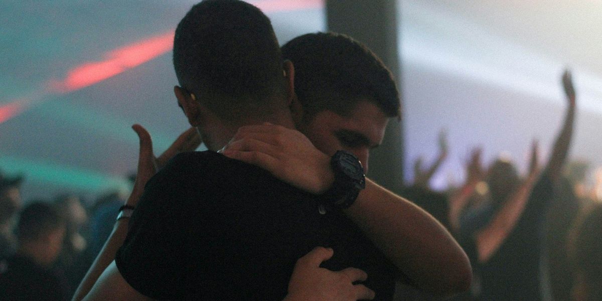 Two young men in a somewhat somber embrace.